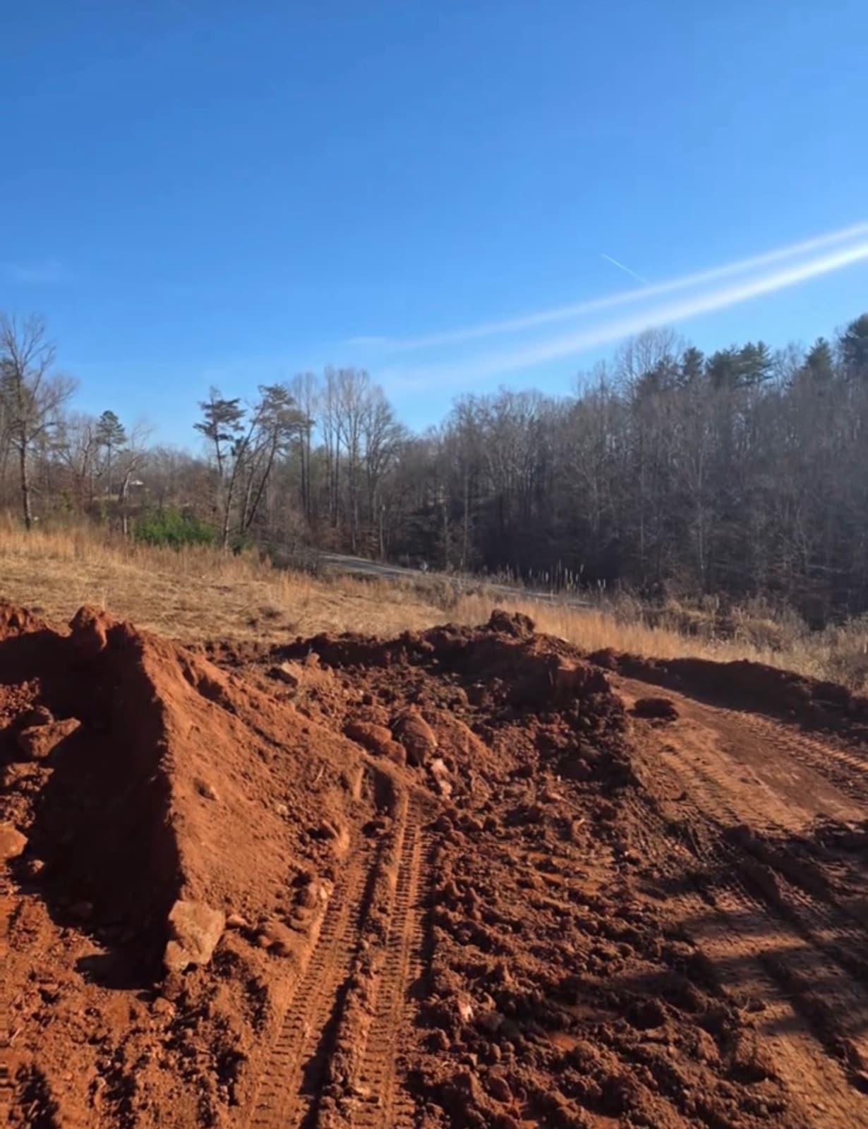 Freshly graded red clay with machine tracks under a clear sky
