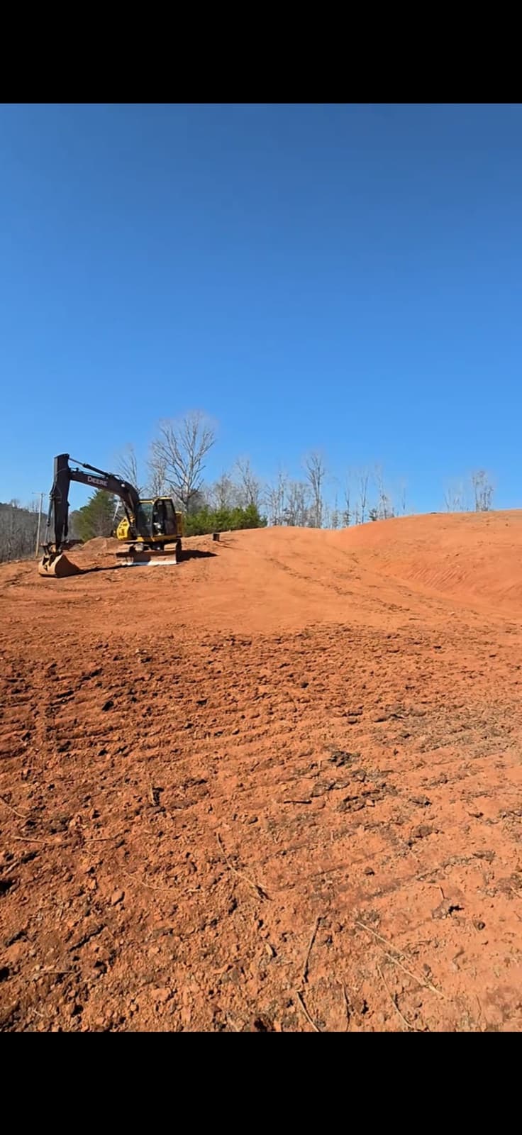 John Deere excavator on a wide graded red clay site