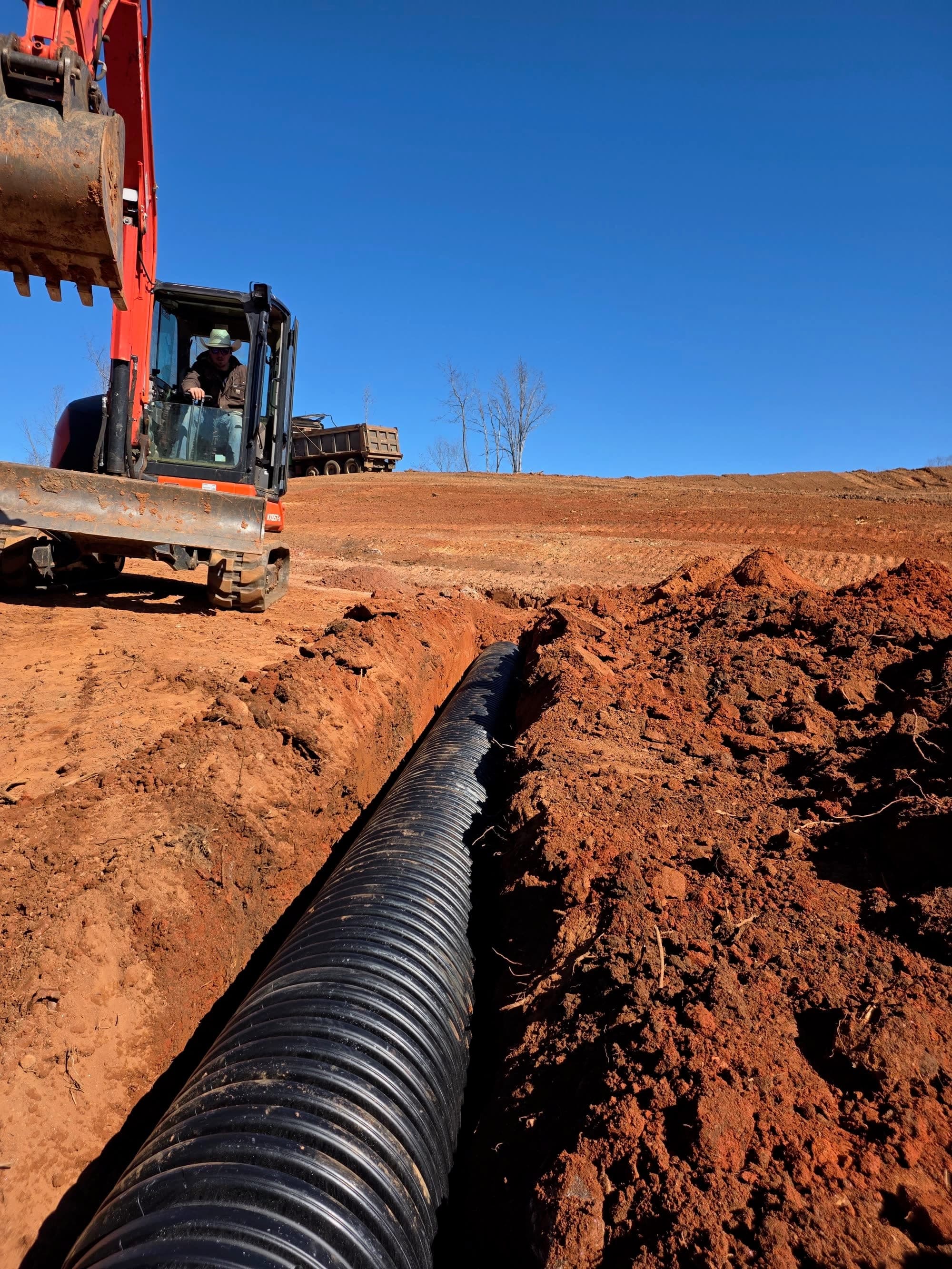 Drainage pipe set in a trench with a dump truck on the hill